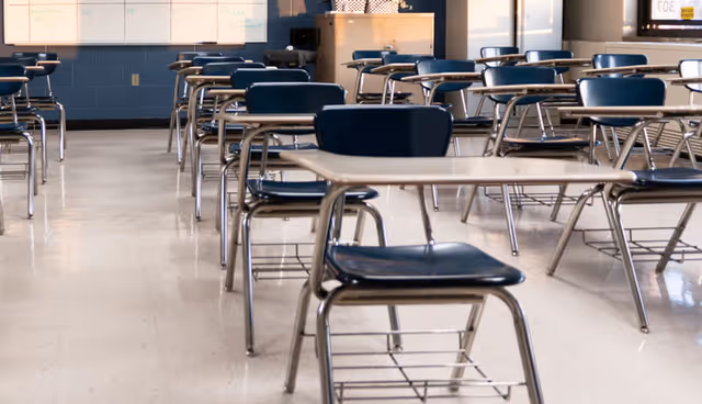 Empty classroom with rows of traditional student desks with attached chairs and shiny tiled floor.